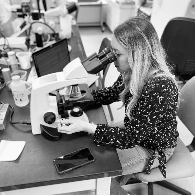 An image of Kylie Hampton at a research laboratory, looking into a microscope. 