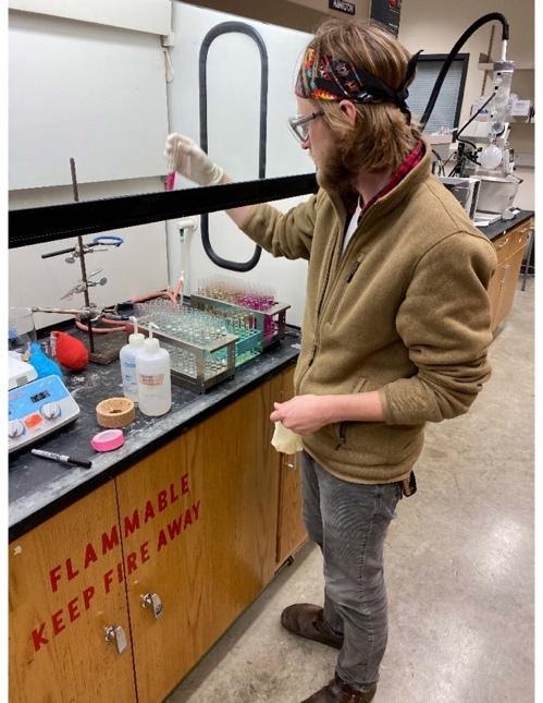 A picture of David pipetting chemicals under a fume hood. 