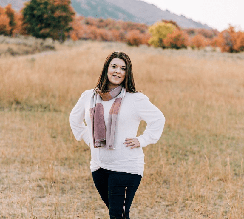 Dr. Jayme Walters stands in a field with a mountain in the backdrop. She has her hands on her hips. 