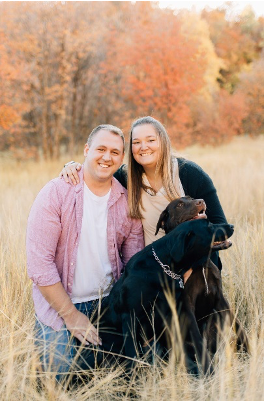A picture of Ragen Dotson. She is posing with a man (likely her romantic partner) and two labradors. Ragen has long blond hair.